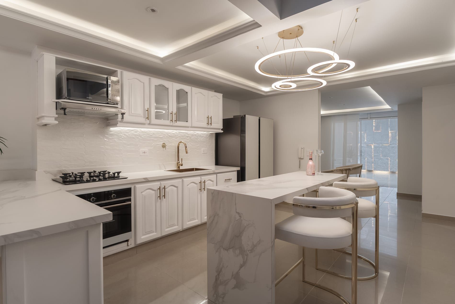 Cocina blanca con isla de mármol y lámpara de anillos dorados