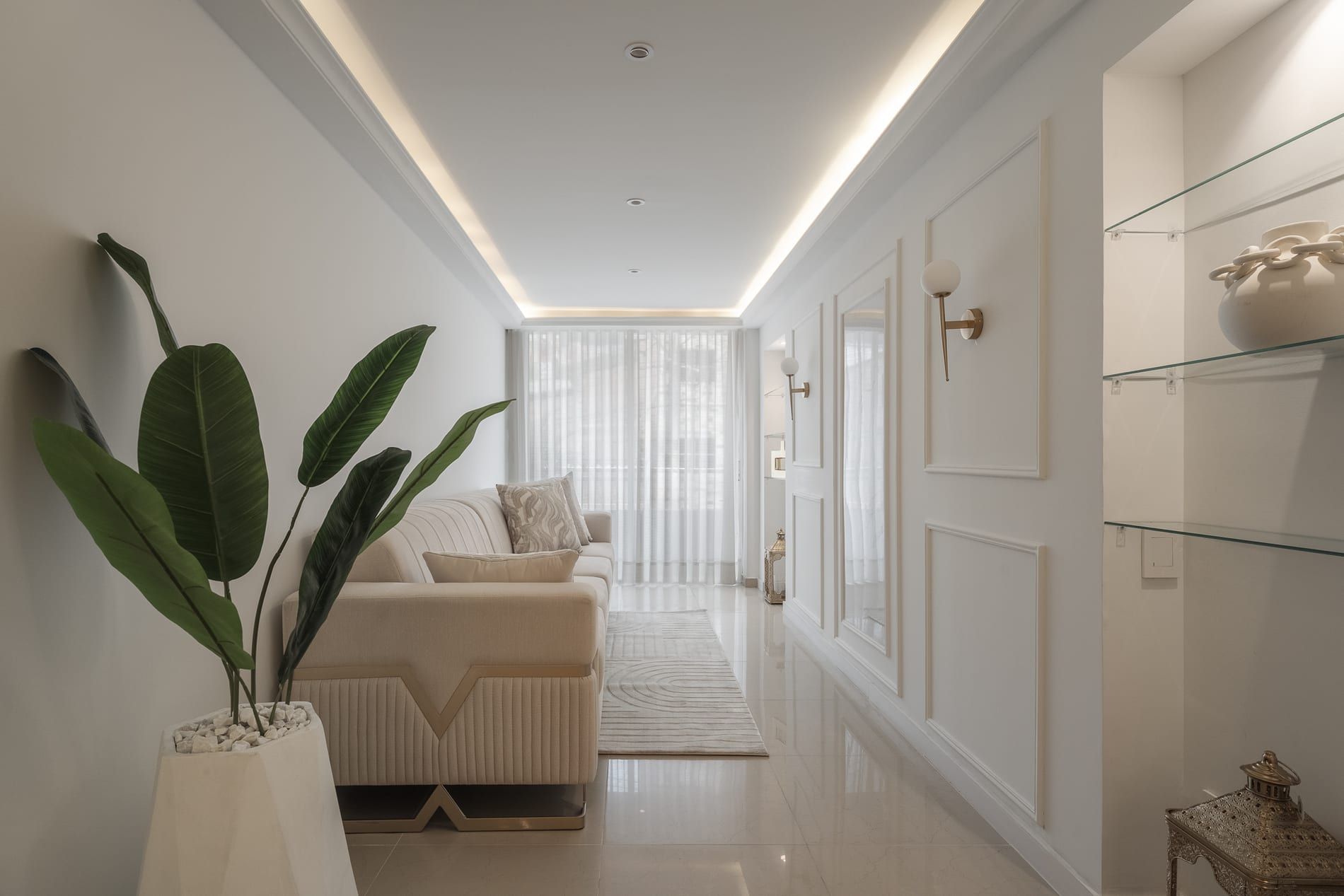 Corredor de la sala con sofá crema, planta y paneles con molduras