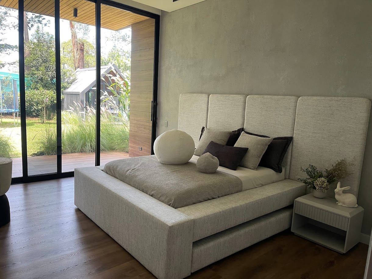 Alcoba con cama tapizada en blanco frente a vidrios hacia el jardín