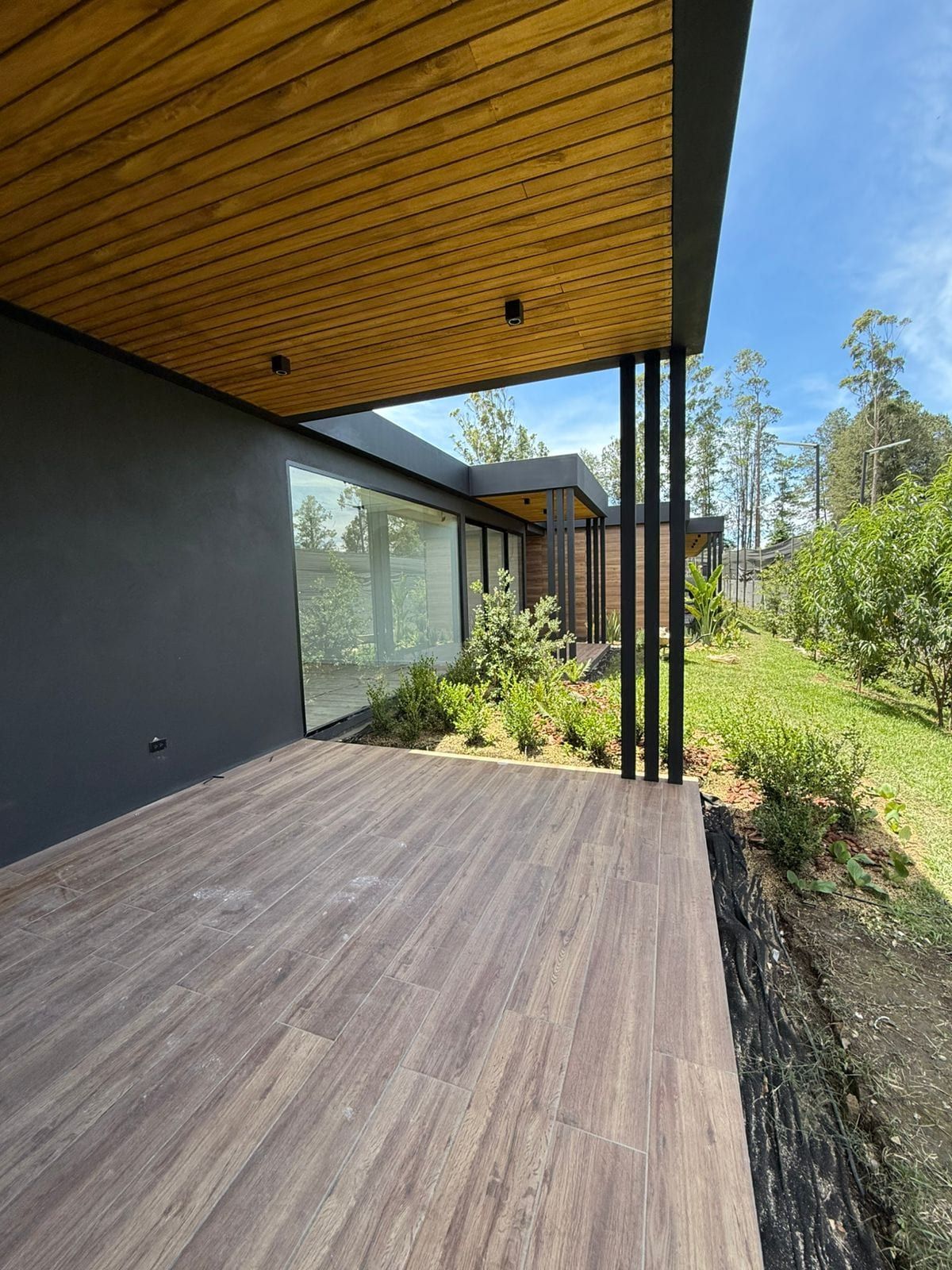 Terraza cubierta con piso y cielorraso de madera frente a un ventanal